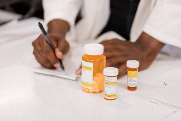 Healthcare professional fills out prescription. Medication bottles sit nearby. Healthcare professional fills out prescription. Medication bottles sit nearby.